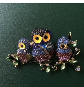 Macro shot of three owls on a branch with colorful crystals and green enamel leaves
