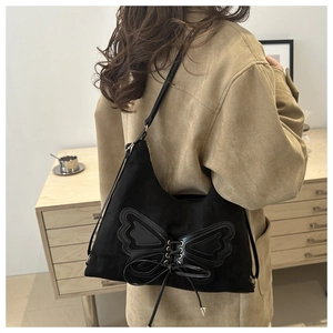 Détail du sac à bandoulière noir mat avec grand nœud papillon sur un manteau kaki