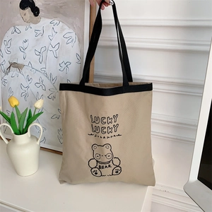 Detail of canvas tote bag with black strap handle and cute bear lucky lucky graphic