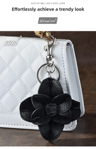 Macro detail of black leather camellia flower keychain with silver hardware on white bag