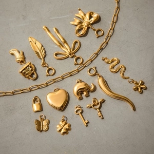 Golden stainless steel necklace set with 14 diverse charms on a grey stone surface