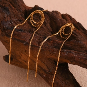 Macro view of golden snake chain fringe earrings hanging on a dark wood display