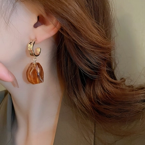 Close-up of amber resin drop earring with gold C-shape stud on model ear