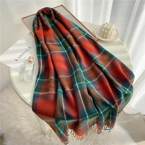 Detailed view of orange and green plaid scarf with fringe tassels on a minimalist table