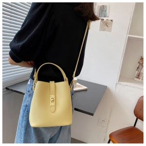 Model wearing a minimalist pale yellow bucket bag with top handle and shoulder strap