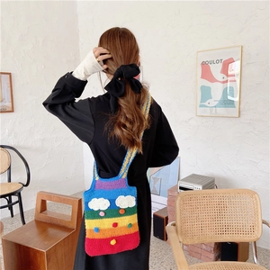 Rainbow knit shoulder bag with clouds and pompoms worn by model in cozy interior