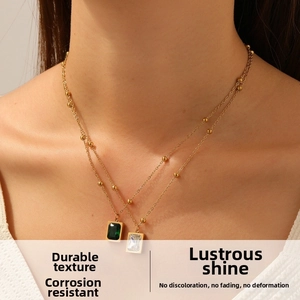Close-up of double-layer gold chain necklace with emerald and clear rectangle pendants