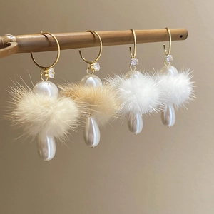 Detail showing plush fur balls and pearl drops on elegant C-shaped silver needle earrings