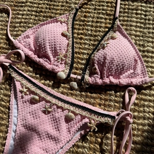 Pink textured bikini set with shell and starfish charms on a woven straw mat backdrop
