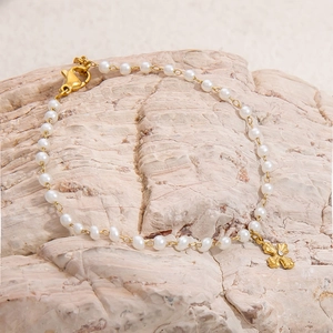 18K gold plated stainless steel pearl bracelet with a cross pendant on a stone background