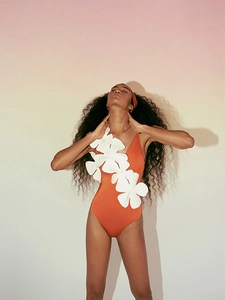Detailed close-up of orange one-piece swimsuit featuring large white 3D floral appliques