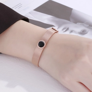 Detail of rose gold mesh bracelet with black circular charm on woman wrist