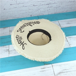Detail of beige straw hat with Hello Sunshine embroidery and frayed fringe edges