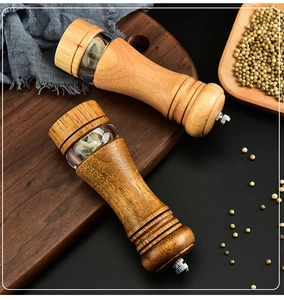 Close-up of manual oak pepper grinders with acrylic window and ceramic core on dark wood