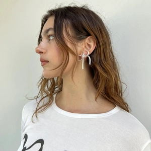 Close-up of a silver bow knot earring on a model, featuring a flat snake chain design