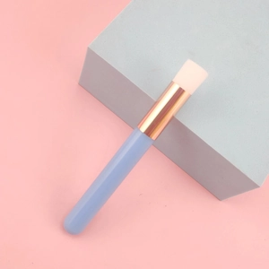 Detail view of a blue eyelash cleansing brush with soft white bristles on a pink surface