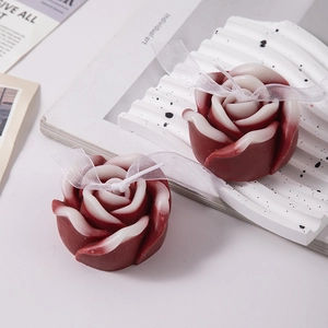 Close-up of rose-shaped scented candles with red gradients and white organza ribbons