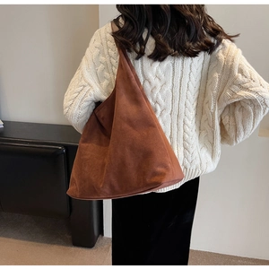 Detailed view of a brown suede tote bag styled with a white sweater in a cozy indoor setting