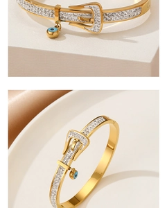 Detailed view of a gold belt buckle bracelet with white zircon and blue evil eye charm