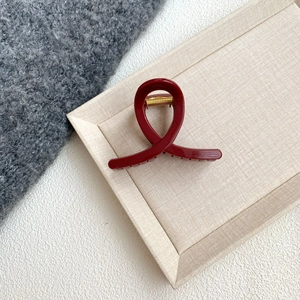 Detail of elegant dark red hair claw clip with gold spring on beige linen tray
