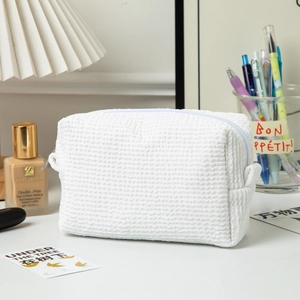 Detail of white waffle texture makeup bag with top zipper closure on a vanity desk