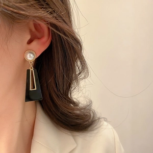 Close-up of geometric black trapezoid drop earrings with gold rim and pearl on model