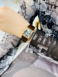Close-up of elegant rectangular gold watch with roman numerals and brown leather strap