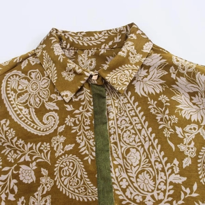 Détail d'une chemise en satin à imprimé paisley avec liseré vert et bouton doré