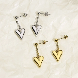 Detail view of heart-shaped drop earrings in gold and silver finish on textured paper