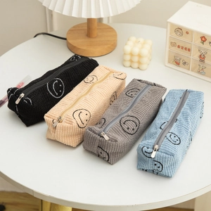 Corduroy smiley face pencil cases in black, beige, grey, and blue on a tidy desk