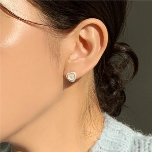 Detail of a 925 sterling silver heart stud earring with white shell inlay worn by a model