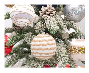 Close-up of white foam Christmas ball with gold glitter swirls on a flocked pine branch