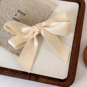 Close-up of elegant beige satin bow hair clip on a soft fabric pad with a wooden tray