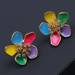 Macro detail of gold flower earrings featuring colorful enamel petals and sparkling rhinestones