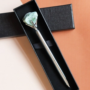 Close-up of a silver metal pen with green raw gemstone crystal in a black gift box