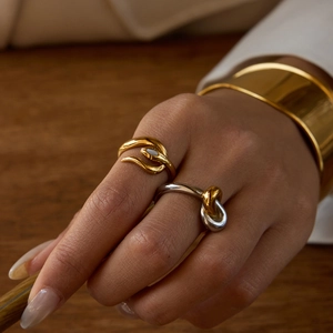 Close-up of gold curved ring with white stone and two-tone knot ring on model's hand