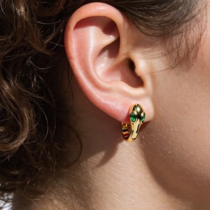 Cool gold snake hoop earrings with green gemstone eyes shown on female model ear