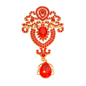 Detailed macro view of vintage gold-plated brooch with red crystals and teardrop pendant
