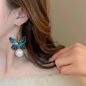 Close-up of elegant teal acrylic butterfly earrings with large white pearls and gold hooks
