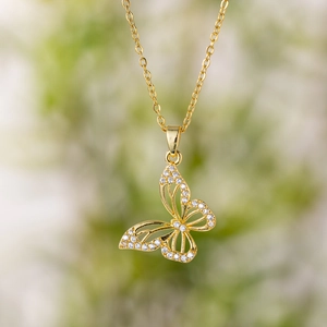 Minimalist gold butterfly pendant necklace with micro-pave crystals on nature background