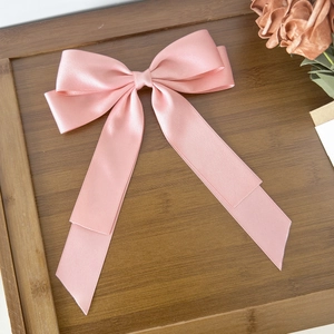 Detail of elegant pink satin bow hair clip placed on a wooden tray with dried flowers