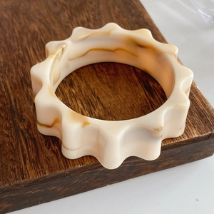 Detail of cream marbled resin bangle with scalloped gear edges on wood stand