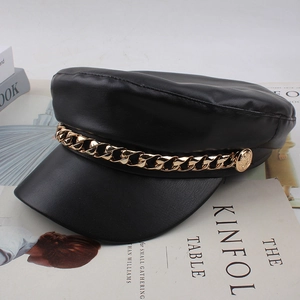 Close-up of matte black leather baker boy hat with a textured gold metal chain detail