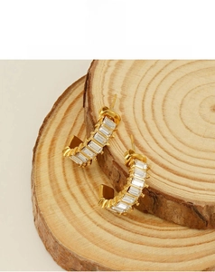 Macro view of gold U-shaped earrings with rectangular cubic zirconia on a wooden base