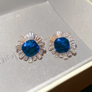 Macro shot of blue zircon starburst stud earrings set in a grey jewelry gift box