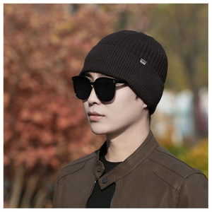 Detail of dark brown knitted beanie with metal logo plate and ribbed texture detail