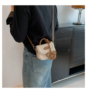 Chic beige crossbody bag with brown handle and cute bear charm shown on a model