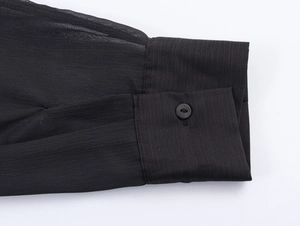Dettaglio del polsino di una camicia in chiffon nero con bottone e trama trasparente