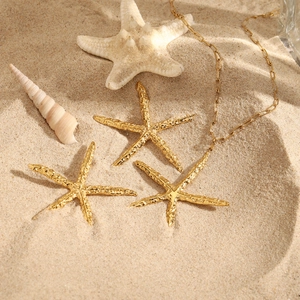 Gold starfish jewelry set with hammered texture and paperclip chain on sand background