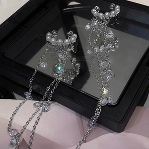 Detail of silver long tassel earrings with sparkling crystals and pearls on black mirror
